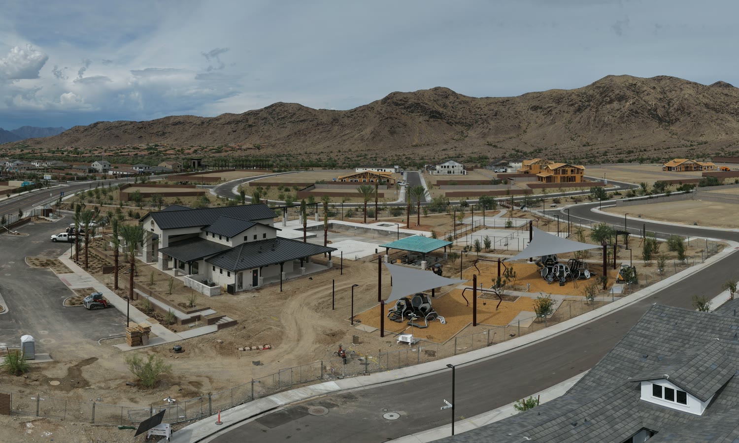 Drone view of the Upper Canyon clubhouse, pool under construction and shaded playgrounds, with South Mountain behind
