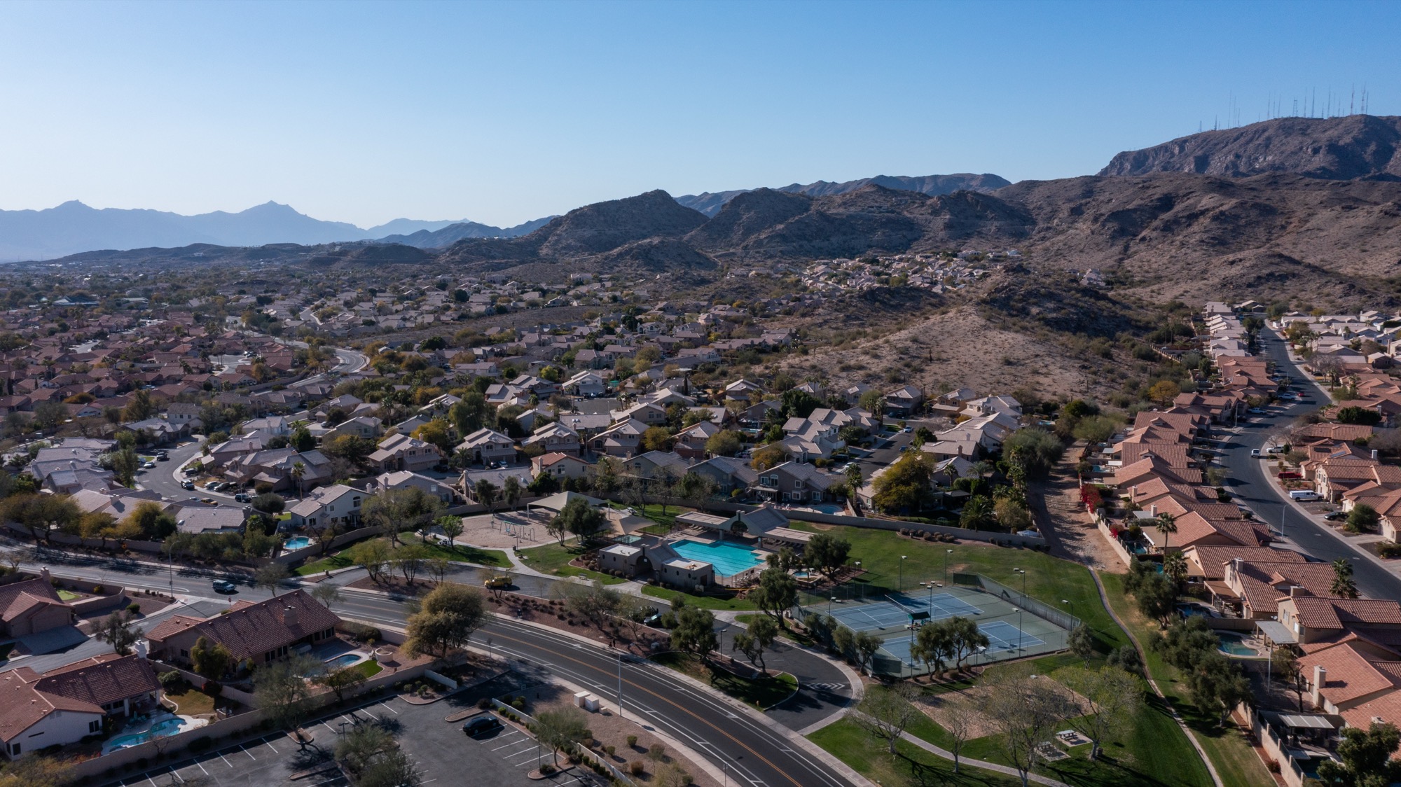 Aerial view over Ahwatukee homes, a community pool and tennis courts, with South Mountain behind