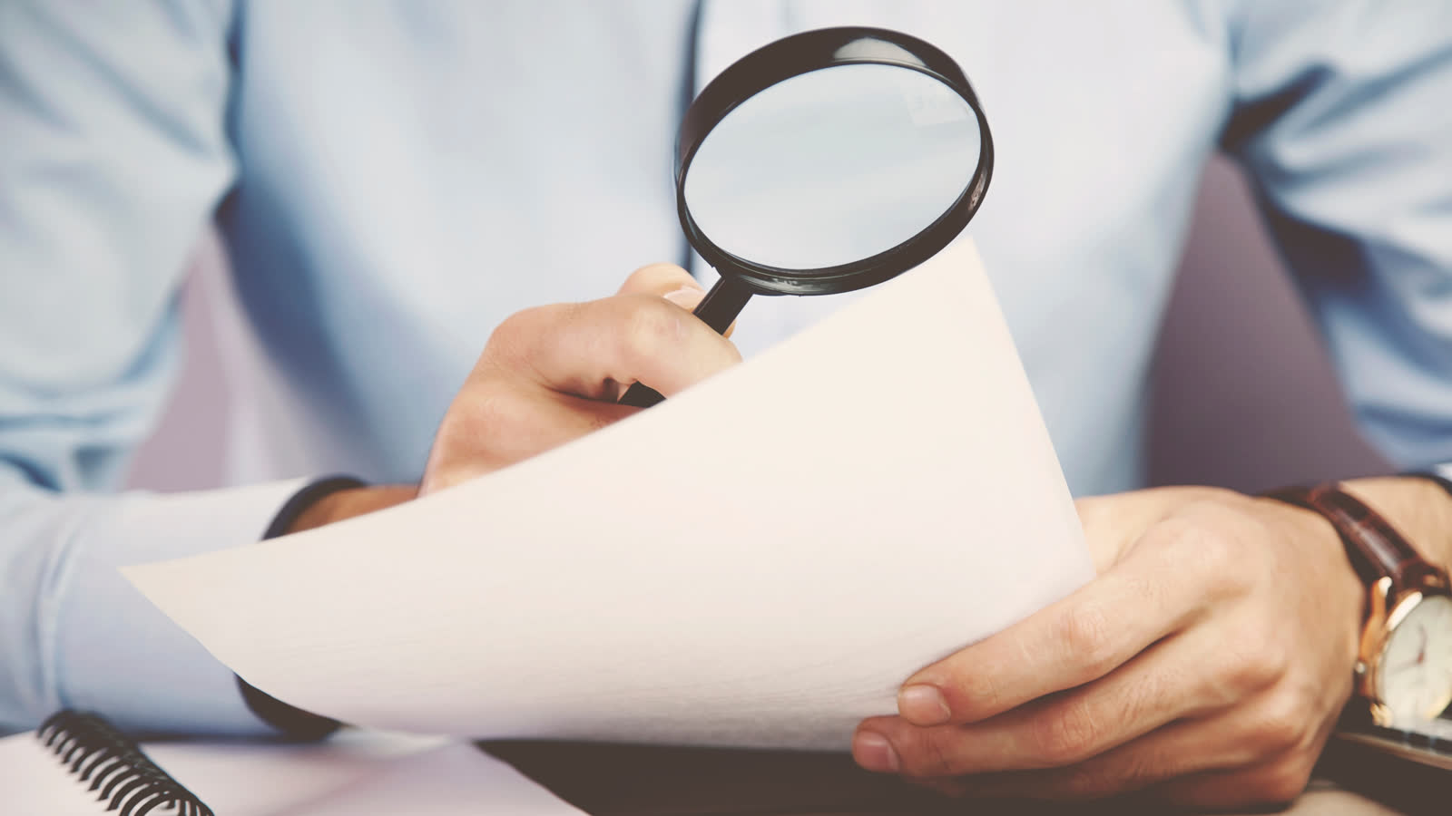 A hand holding a magnifying glass over printed text