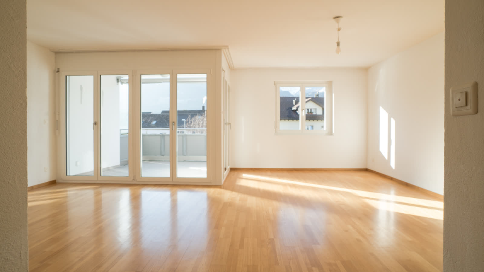 A bright empty living room with wooden floors and french doors