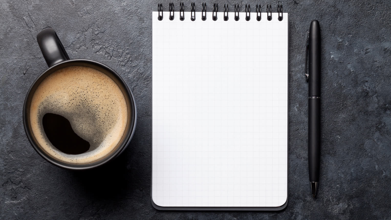 A notepad and pen on a desk beside a cup of coffee